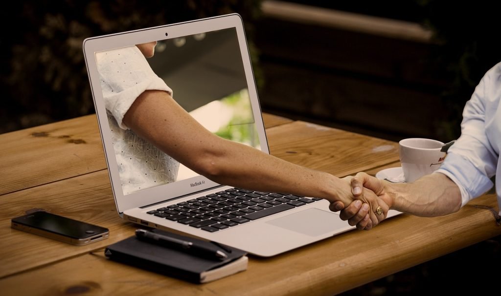 "Stretta di mano virtuale tra due persone attraverso uno schermo di laptop, simbolo di counseling online e connessione digitale."